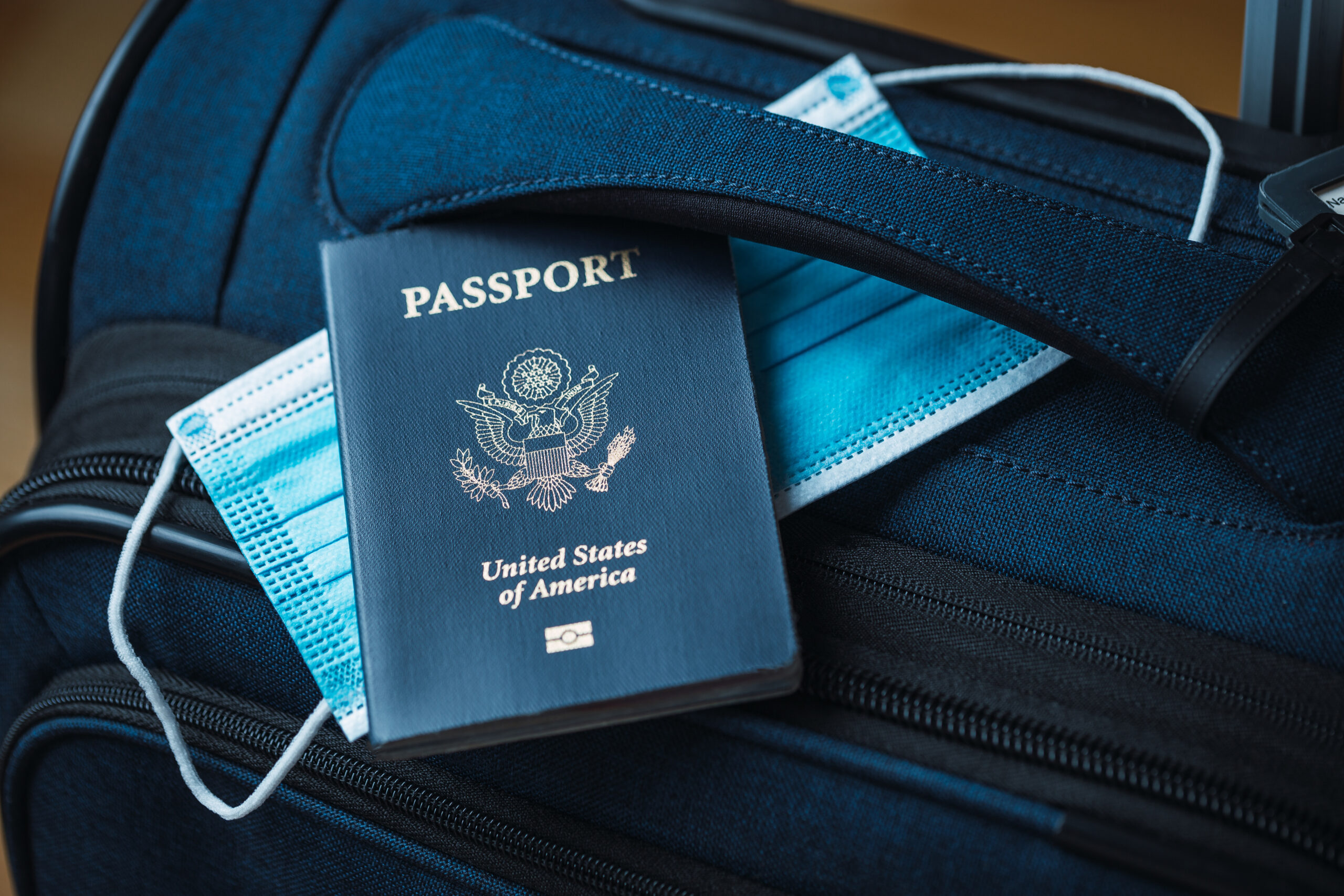 A suitcase with a mask lying on top. An American passport sits on top of the mask and suitcase.